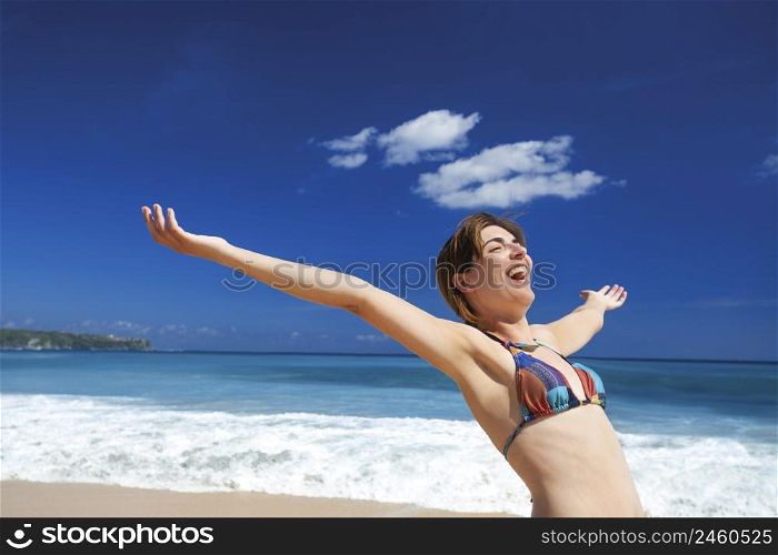 Beautiful young woman with arms open in a tropical beach enjoying the summer