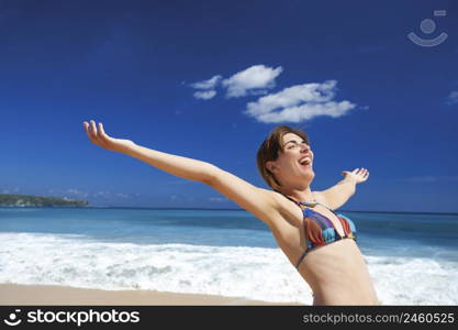 Beautiful young woman with arms open in a tropical beach enjoying the summer