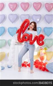 beautiful young woman with balloon in the form of a love in hands on many colorful heart balloons background. smiles,funny Valentine s Day birthday party. beautiful young woman with balloon in the form of a love in hands on many colorful heart balloons background. smiles,funny Valentine s Day birthday party.