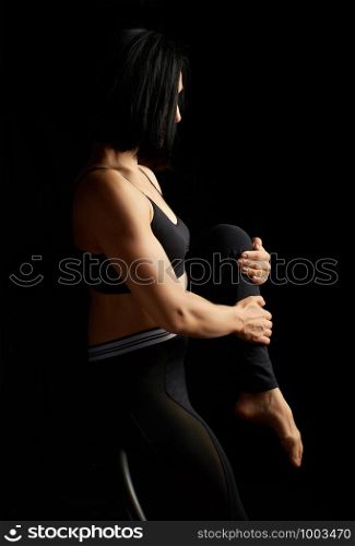 beautiful young woman with black hair and a muscular body sits on a sports simulator and performs an exercise, low key