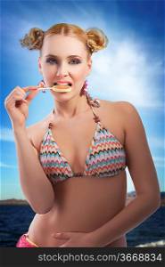 beautiful young woman with blond hair and stylish in bikini swimsuit eating candy