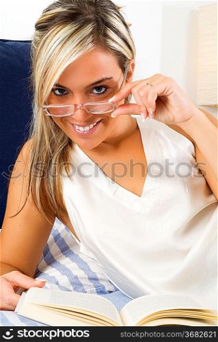 beautiful young woman with blond hair reading a book one evening in bed before to sleep