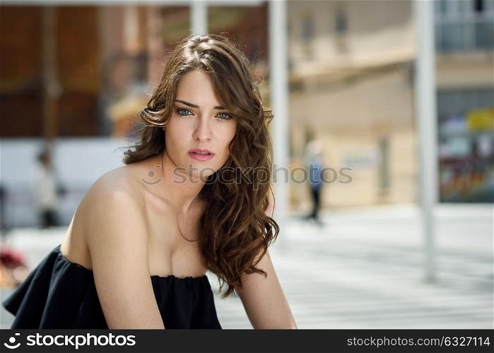 Beautiful young woman with blue eyes and long hair in urban background. Girl wearing summer clothes. Curly hairstyle.