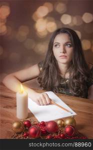 Beautiful young woman, with blue eyes, thinking what to write, at candlelight, surrounded by red and yellow globes and Christmas lights.