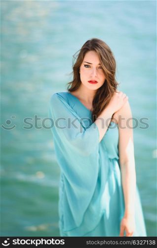 Beautiful young woman with blue eyes wearing blue dress in the beach.