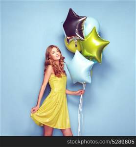 Beautiful young woman with colorful balloons on a blue background. Birthday and party. Girl in green dress at the festival