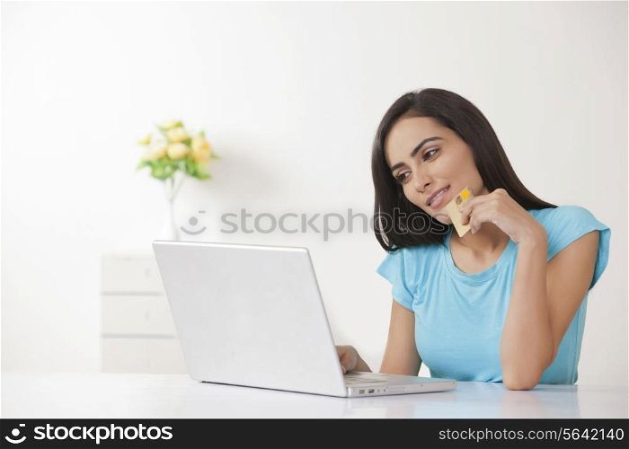 Beautiful young woman with credit card shopping online at home