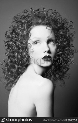 Beautiful young woman with curly-hair on grey background. Nude pretty lady with dark black lipsstick and modern art makeup. Sensual model pose in photo-studio. Sexy naked body.