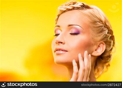 Beautiful young woman with hairdo touching her face with hand