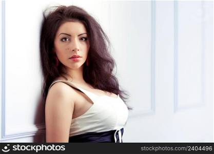 Beautiful young woman with long dark hair lean against white wall
