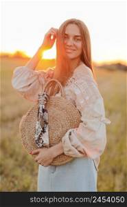 beautiful young woman with long hair and straw bag in hand in the summer at sunset in the field for a walk. she is happy. background blurred art photography. summer holiday concept. beautiful young woman with long hair and straw bag in hand in the summer at sunset in the field for a walk. she is happy. background blurred art photography. summer holiday concept.