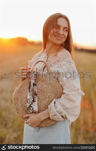 beautiful young woman with long hair and straw bag in hand in the summer at sunset in the field for a walk. she is happy. background blurred art photography. summer holiday concept. beautiful young woman with long hair and straw bag in hand in the summer at sunset in the field for a walk. she is happy. background blurred art photography. summer holiday concept.