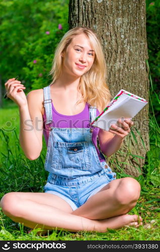 beautiful young woman with note pad sitting on the lawn