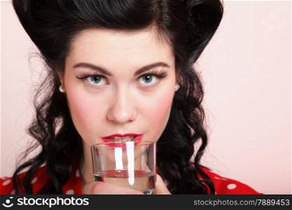 Beautiful young woman with pinup makeup and hairstyle drinking water pink background