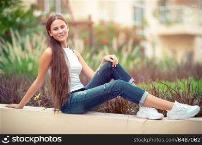 Beautiful young woman with pleasure spending time outdoors, student girl with natural makeup resting in the park, genuine womens beauty. Beautiful young woman outdoors