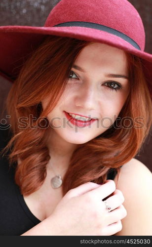 Beautiful young woman with red hair wearing a floppy hat smiling