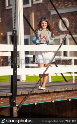 Beautiful young woman with tablet walking on wooden bridge at european city