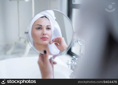 Beautiful young woman with towel on her head looking in the mirror