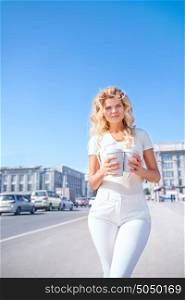 Beautiful young woman with two takeaway coffee cups, standing against urban city background and looking aside.