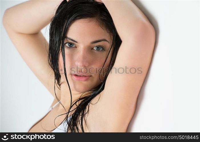 Beautiful young woman with wet hair leaning on white wall after shower or bath in bathroom