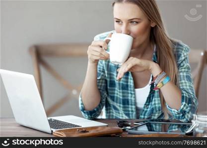Beautiful Young Woman Working from Home. Pretty Female with Pleasure Drinking Coffee and Working on the Laptop. Freelancing.