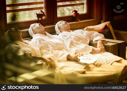 beautiful young women getting facial clay mask at spa, lying with cucumbers on eyes