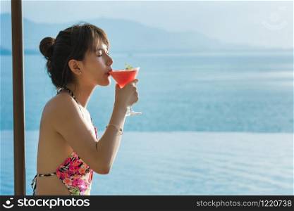 Beautiful young women in bikini lying on a deckchair pool with a red drink looking view by the sea