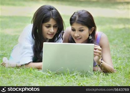 Beautiful young women lying on grass and using laptop