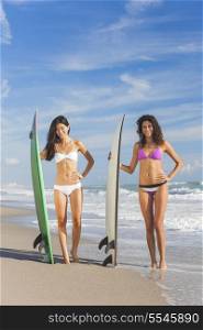 Beautiful young women surfer girls in bikinis with surfboards on a beach