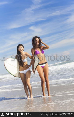 Beautiful young women surfer girls in bikinis with surfboards standing in the sea laughing on a sunny beach