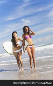 Beautiful young women surfer girls in bikinis with surfboards standing in the sea laughing on a sunny beach