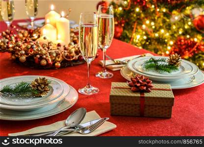 Beautifully decorated Christmas table - gift, glasses of champagne and tableware with Christmas decoration on a red tablecloth.