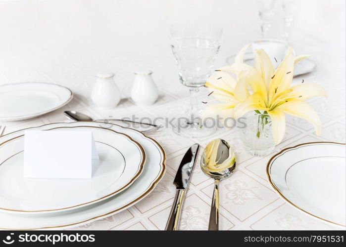 Beautifully decorated table with white plates, crystal glasses, cutlery and flowers on luxurious tablecloths, with guest card