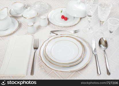 Beautifully decorated table with white plates, crystal glasses, linen napkin, cutlery and cherry berries on luxurious tablecloths