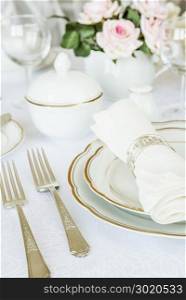 Beautifully decorated table with white plates, glasses, cutlery and flowers on luxurious tablecloths