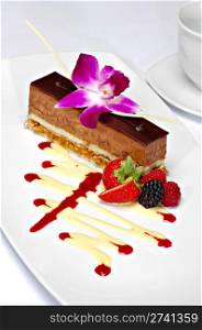 Beautifully plated chocolate mousse cake garnished with a purple orchid, strawberry, blackberry and raspberry. A zigzag of white chocolate and strawberry sauce completes the plate.