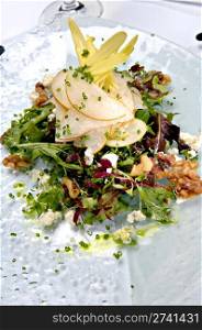 Beautifully plated fresh mixed green salad with pears, walnuts and goat cheese. This salad is served on a glass plate.