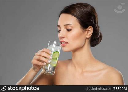 beauty and detox concept - woman drinking fresh water with cucumber and ice over grey background. woman drinking water with cucumber and ice
