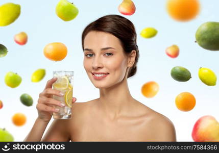 beauty and detox concept - woman drinking fresh water with lemon and ice over fruits on blue background. woman drinking water with lemon and ice