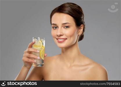 beauty and detox concept - woman drinking fresh water with lemon and ice over grey background. woman drinking water with lemon and ice