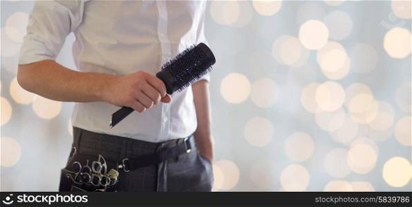 beauty and hair salon, hairstyle and people concept - close up of male stylist with brush at salon over blank holidays lights background