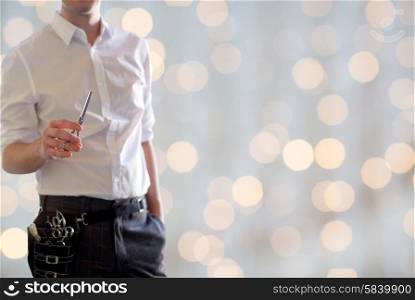 beauty and hair salon, hairstyle and people concept - close up of male stylist with scissors over blank holidays lights background