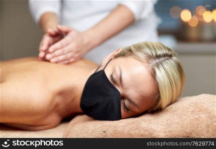 beauty and health safety concept - close up of woman wearing face medical mask lying with closed eyes and having hand massage in spa. close up of woman lying and having massage in spa