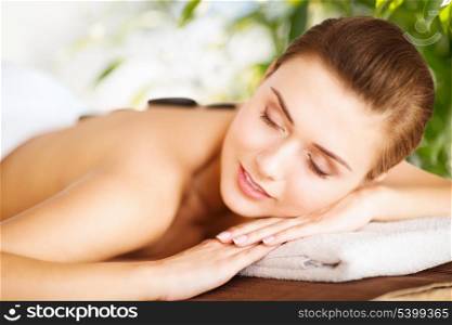 beauty and holidays concept - woman in spa salon with hot stones