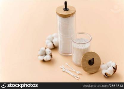 beauty and hygiene concept - close up of cotton pads and swabs in holders on beige background. white cotton pads and swabs in holders