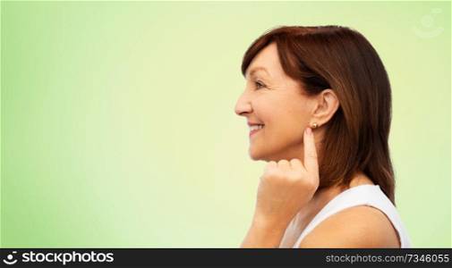 beauty and old people concept - profile of smiling senior woman pointing to her golden earring over lime green natural background. smiling senior woman pointing to her earring