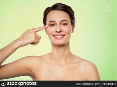 beauty and people concept - beautiful young woman with bare shoulders pointing to her eye over lime green natural background. beautiful young woman pointing to her eye