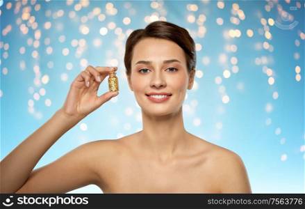 beauty and people concept - beautiful young woman with gold facial mask in bottle over holidays lights on blue background. beautiful young woman with gold facial mask
