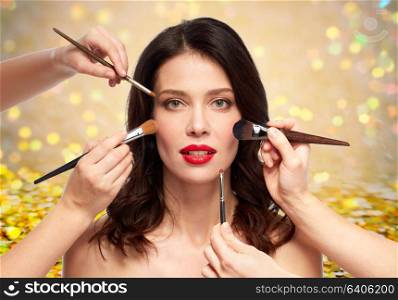 beauty and people concept - beautiful young woman with red lipstick and hands of make up artists with brushes over white background. woman and hands of make up artists with brushes