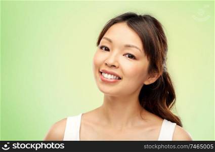 beauty and people concept - face of happy smiling young asian woman over lime green natural background. face of happy smiling young asian woman